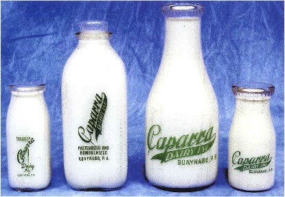 Foto histórica de cuatro botes de leche de cristal de la leche Caparra Dairy en Guaynabo